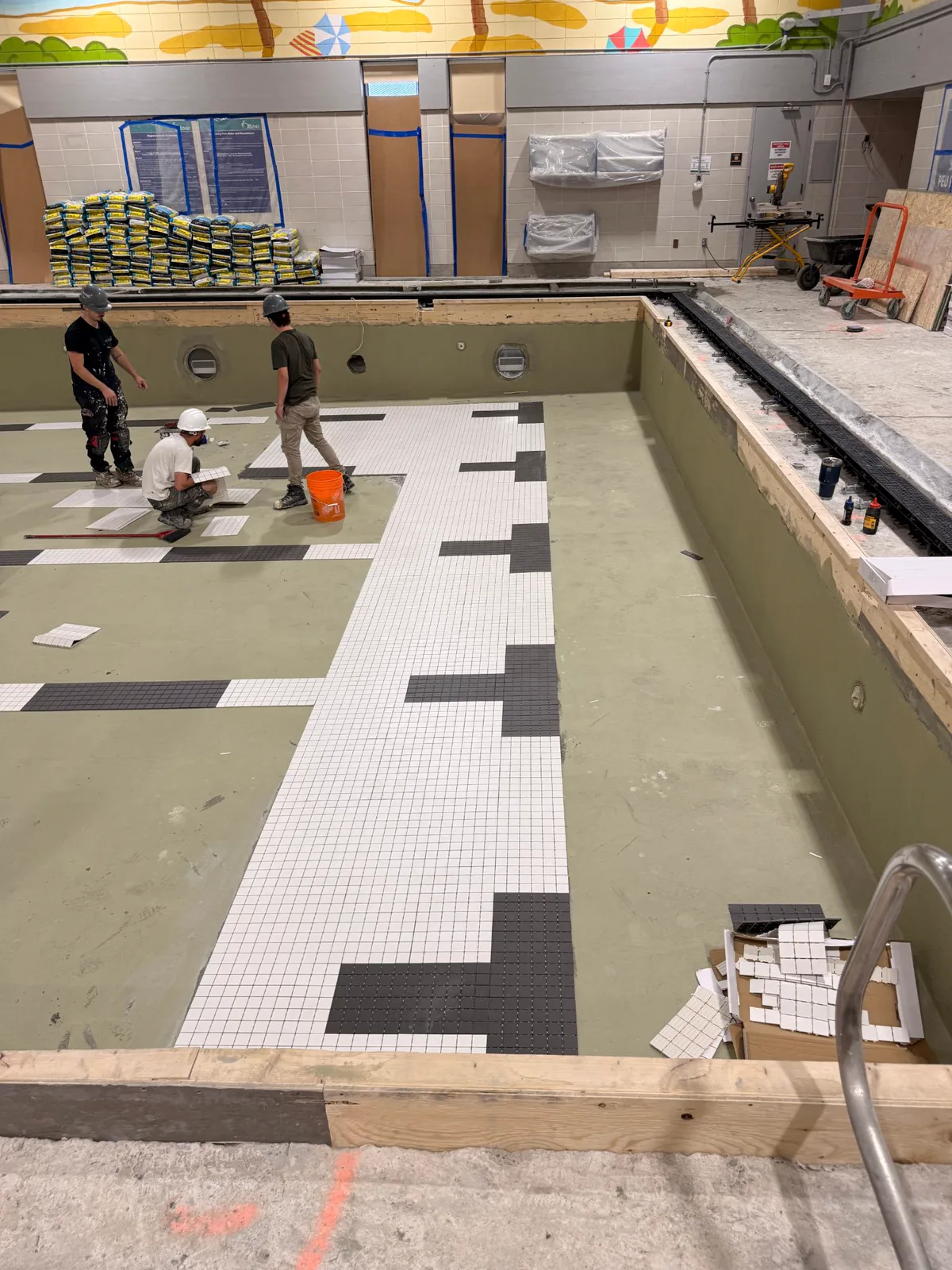 Installers laying white and black mosaic tile over the waterproofing